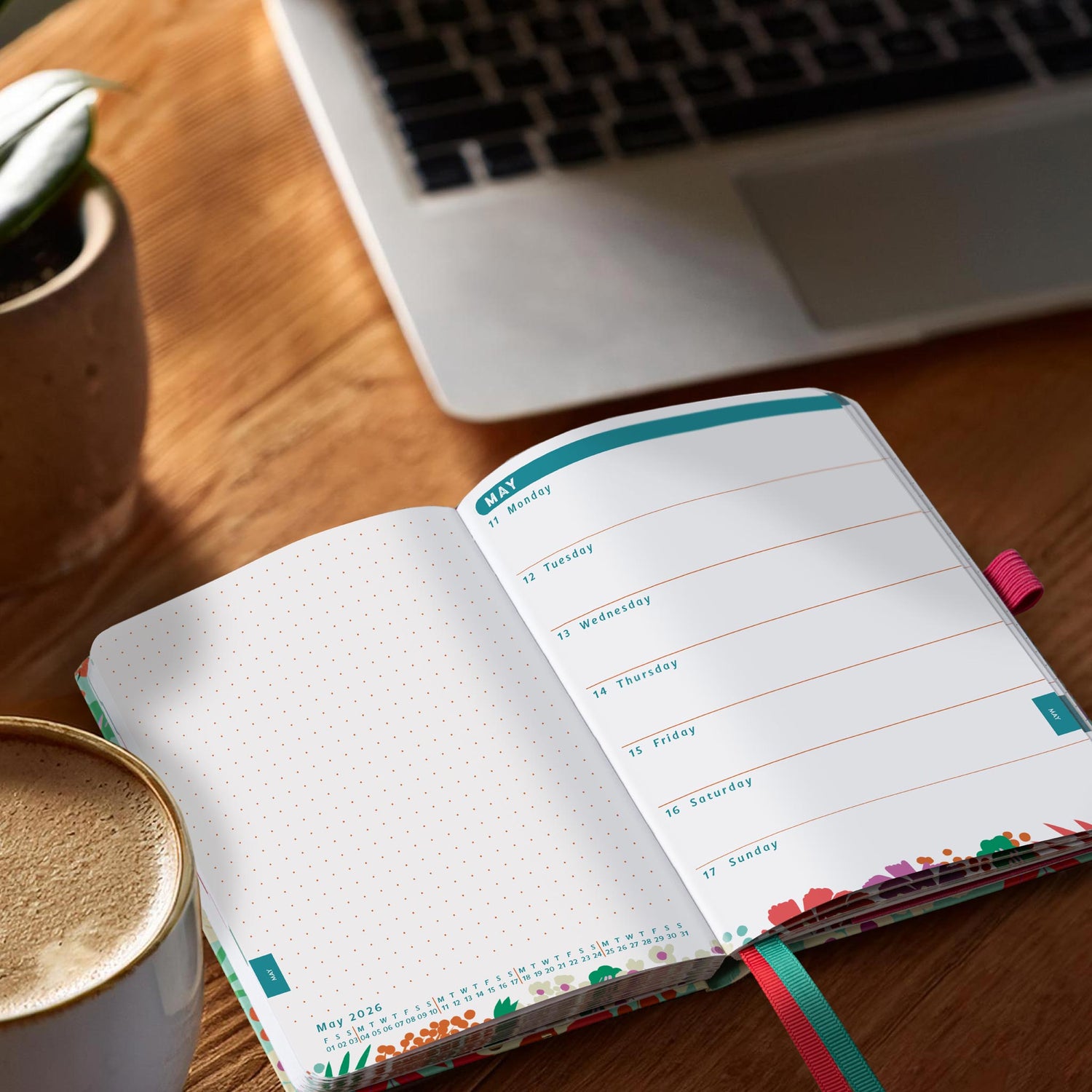 Open diary planner on a desk next to a coffee and a plant in a stone pot.