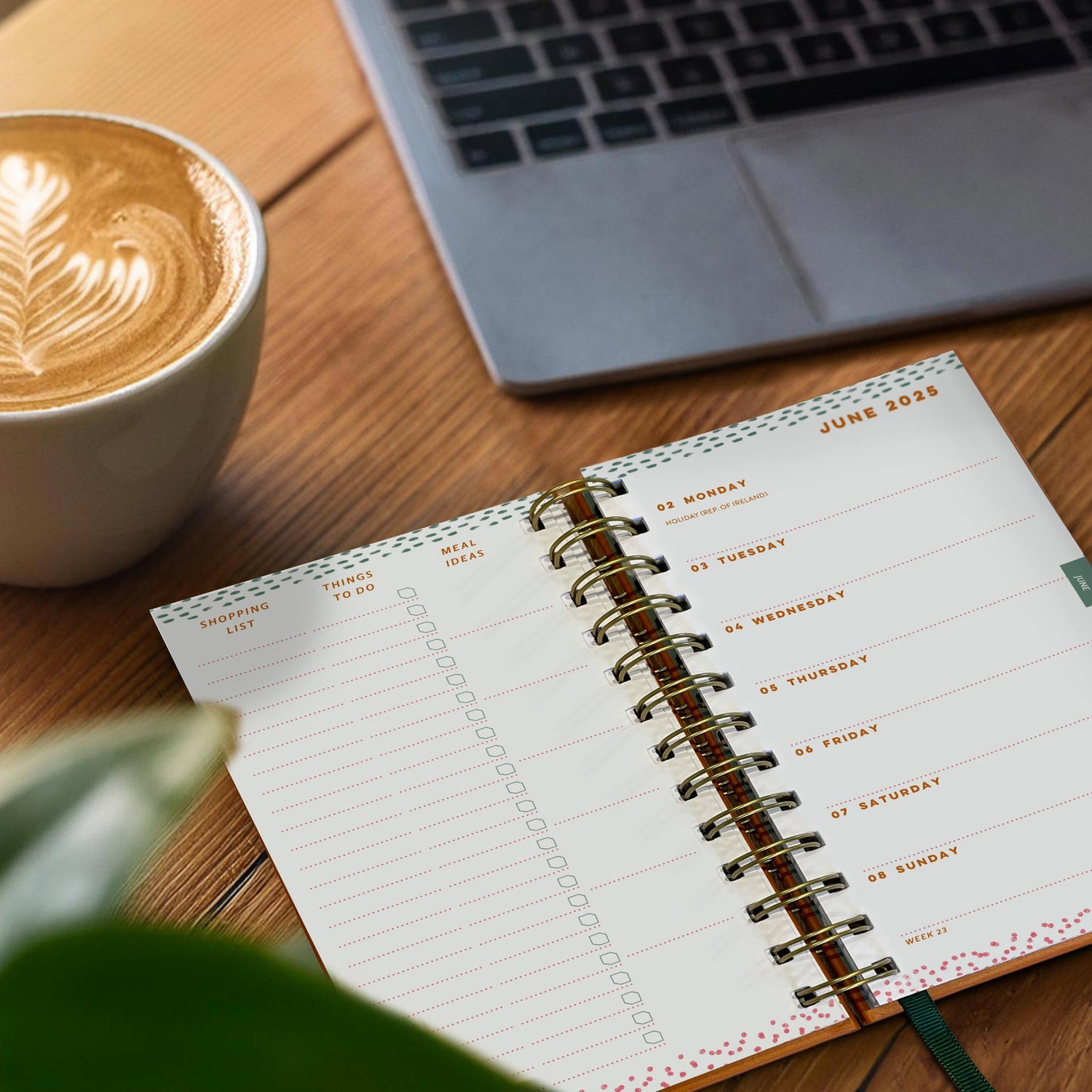 Open pocket diary on a wooden table next to a cappuccino and laptop.