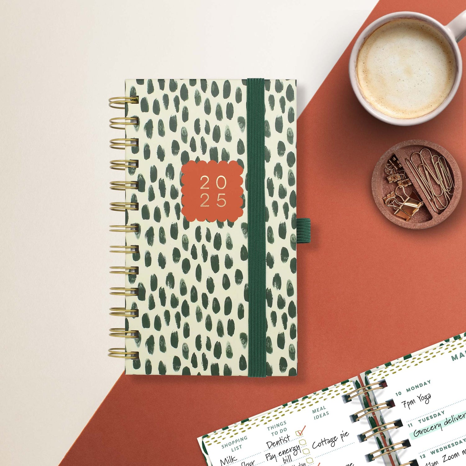 A spiral bound, pocket sized weekly planner in a white cover with green spots
