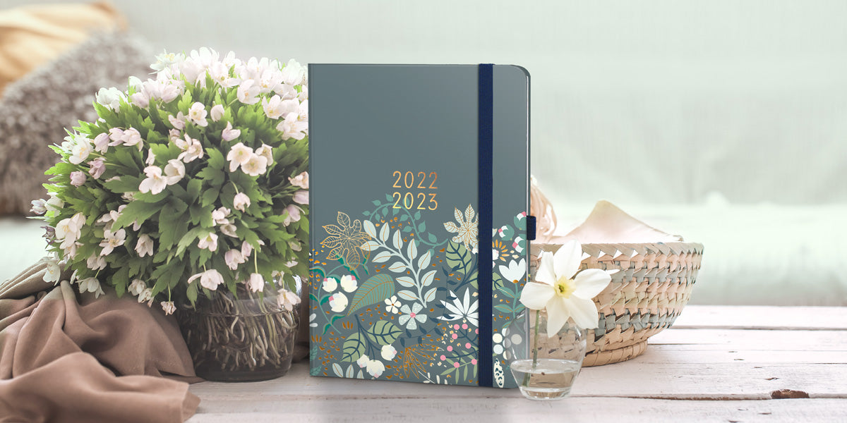 The Enjoy Everyday Academic A5 Diary on a wooden table next to a vase of white flowers