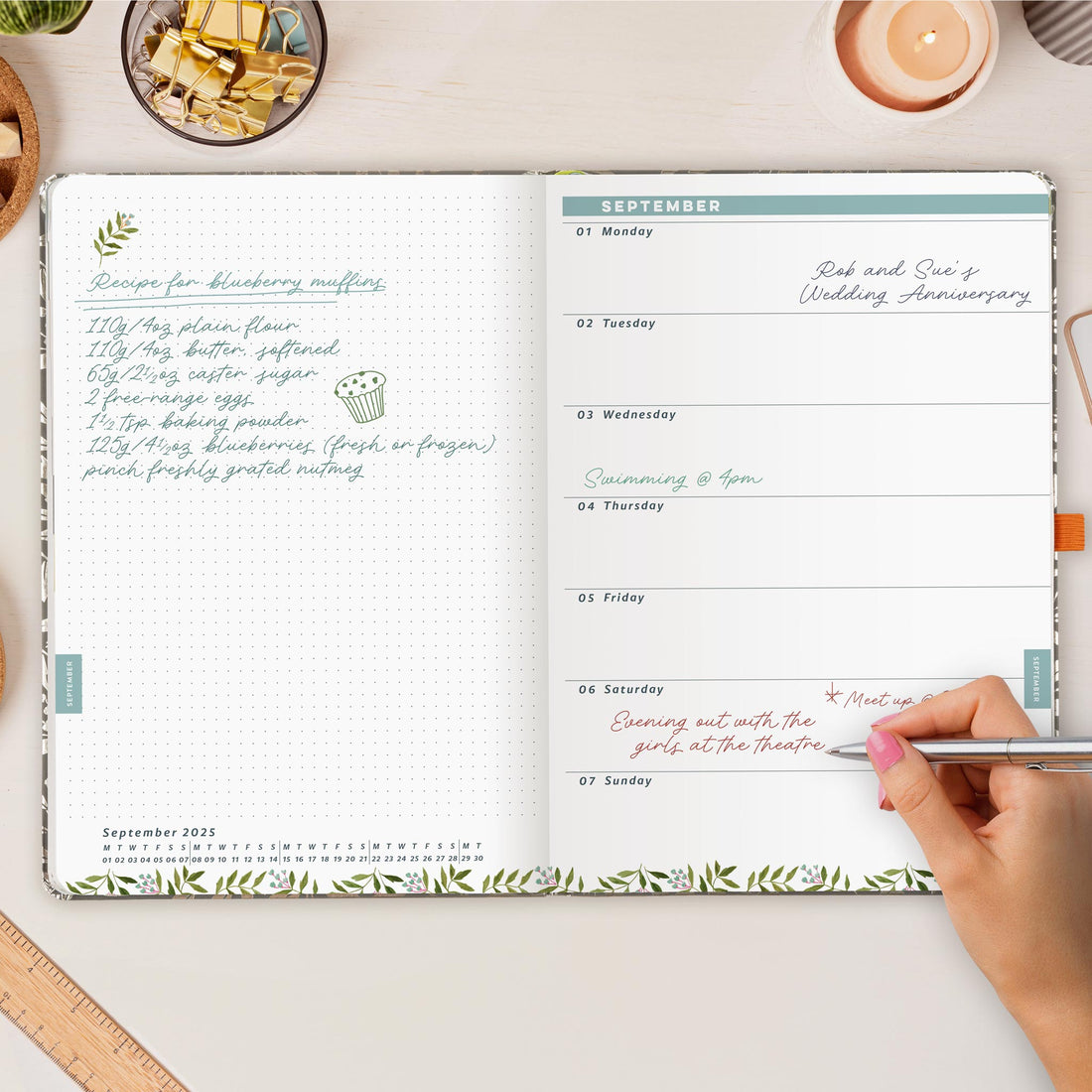 Open desk diary on a white wooden desk with a hand writing in appointments. 
