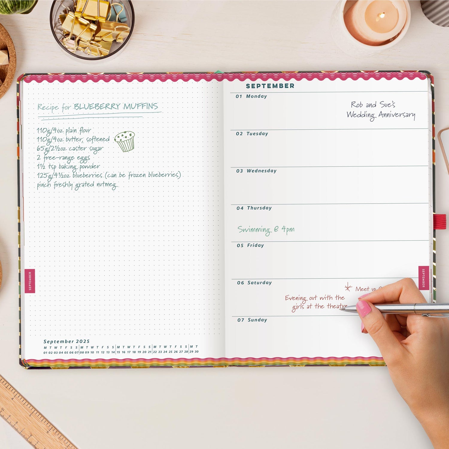 Open desk diary on a white wooden desk with a hand writing in appointments. 