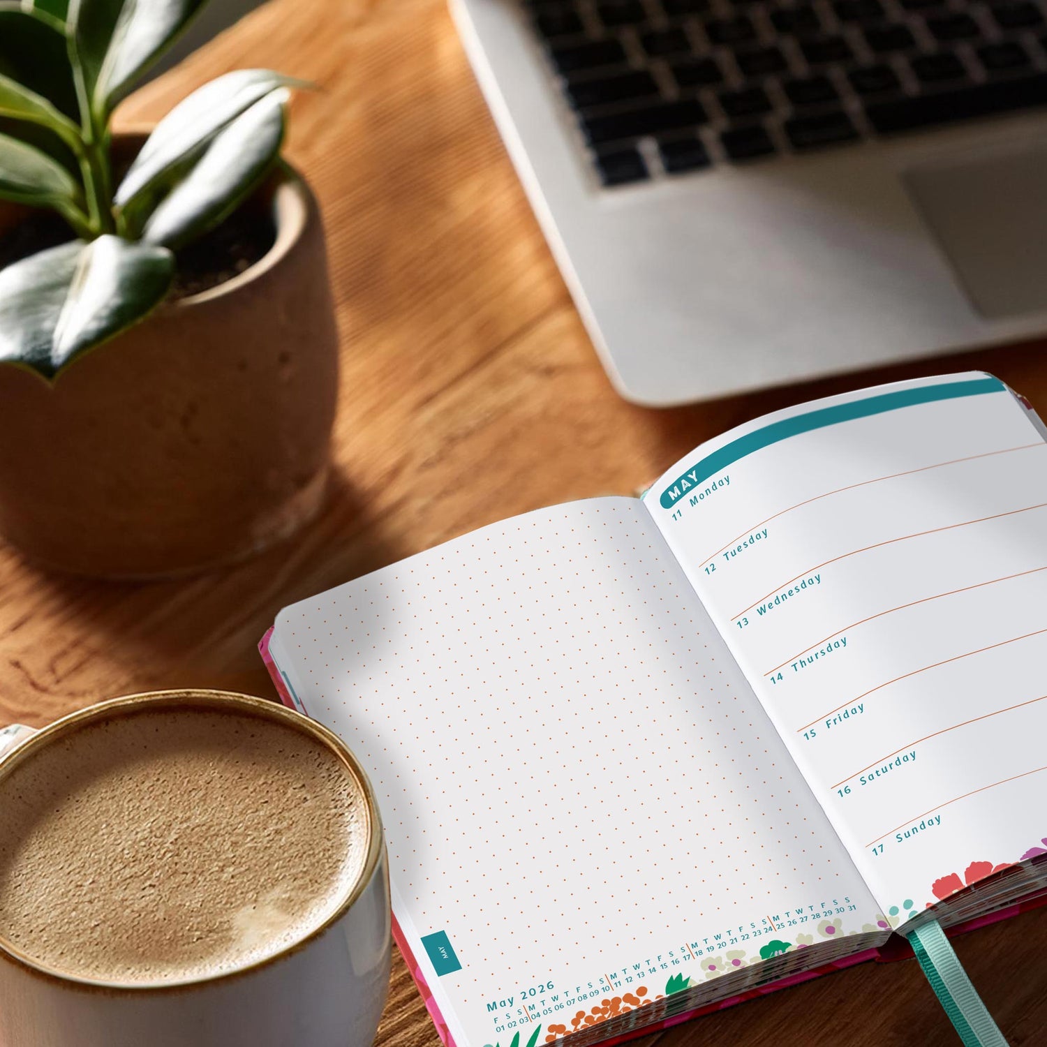 Open diary planner on a desk next to a coffee and a plant in a stone pot. 
