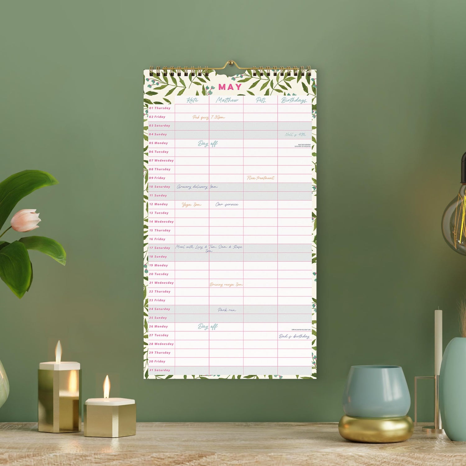 Wall calendar with a 4 column layout and leaf design hung on a green wall. 