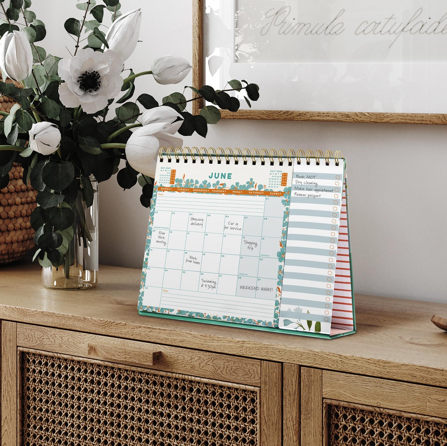 Desk Calendar with Flip Pad 2025 on a wooden table next to a vase of white flowers. 