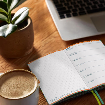 Open Everyday weekly diary on a desk next to a coffee and a plant in a stone pot. 