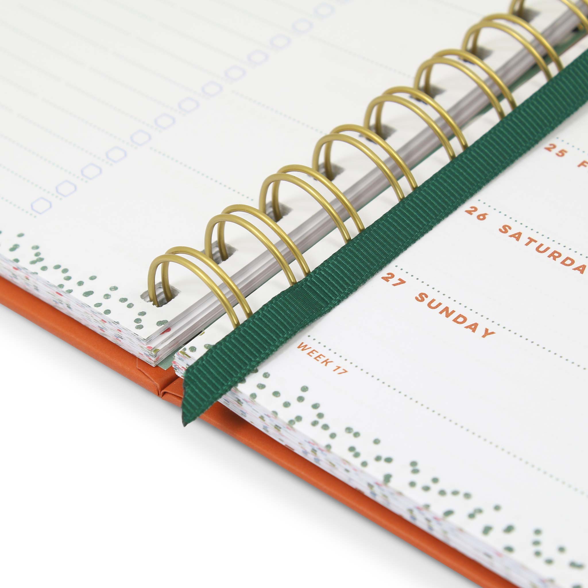 A close up of a pocket weekly planner with gold spiral binding and a green ribbon page marker