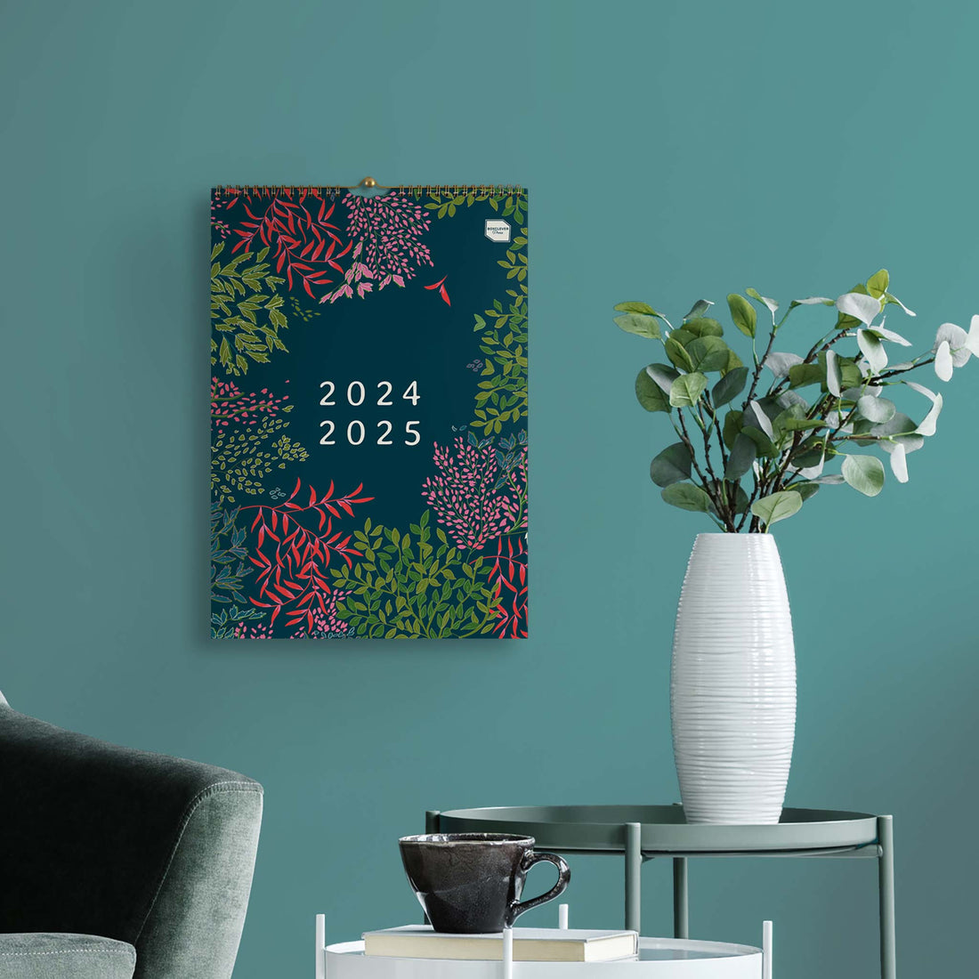 Large wall calendar hanging on a blue wall with a vase of flowers in front