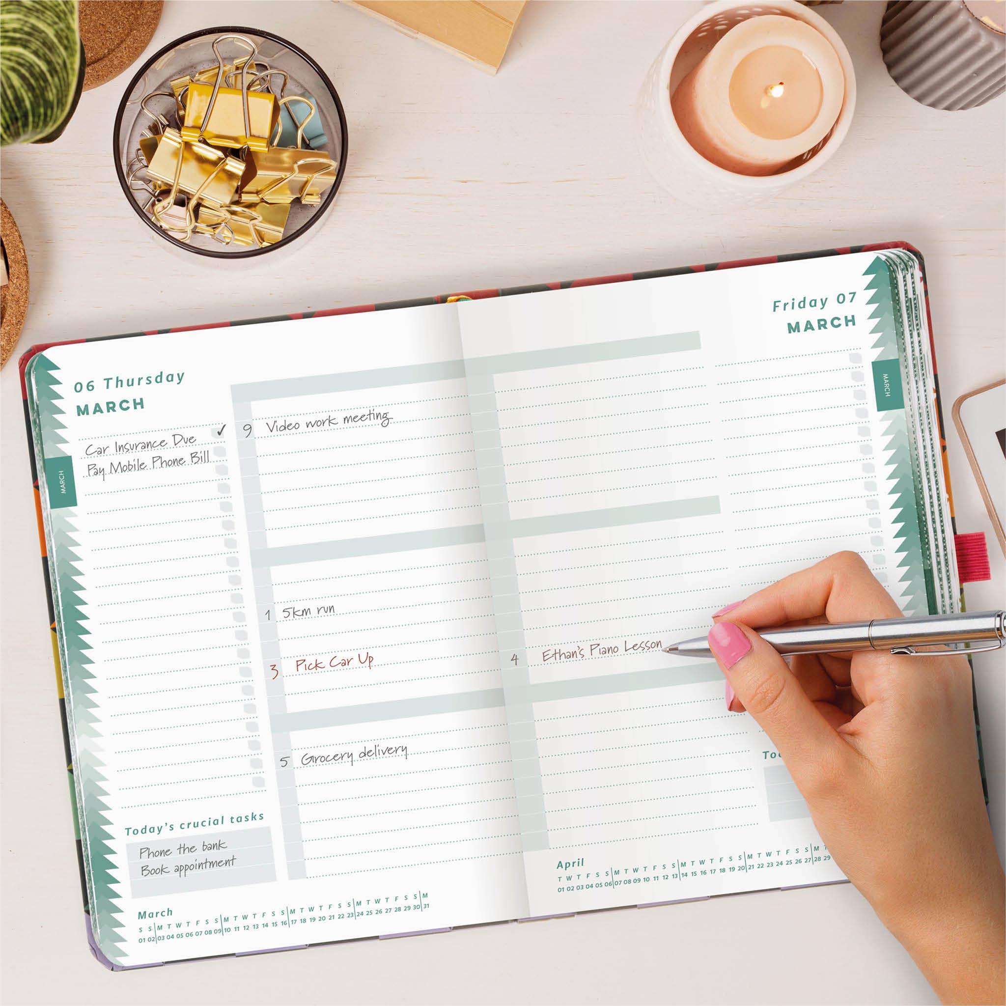 Open daily planner on a wooden table with a hand writing in appointments. 