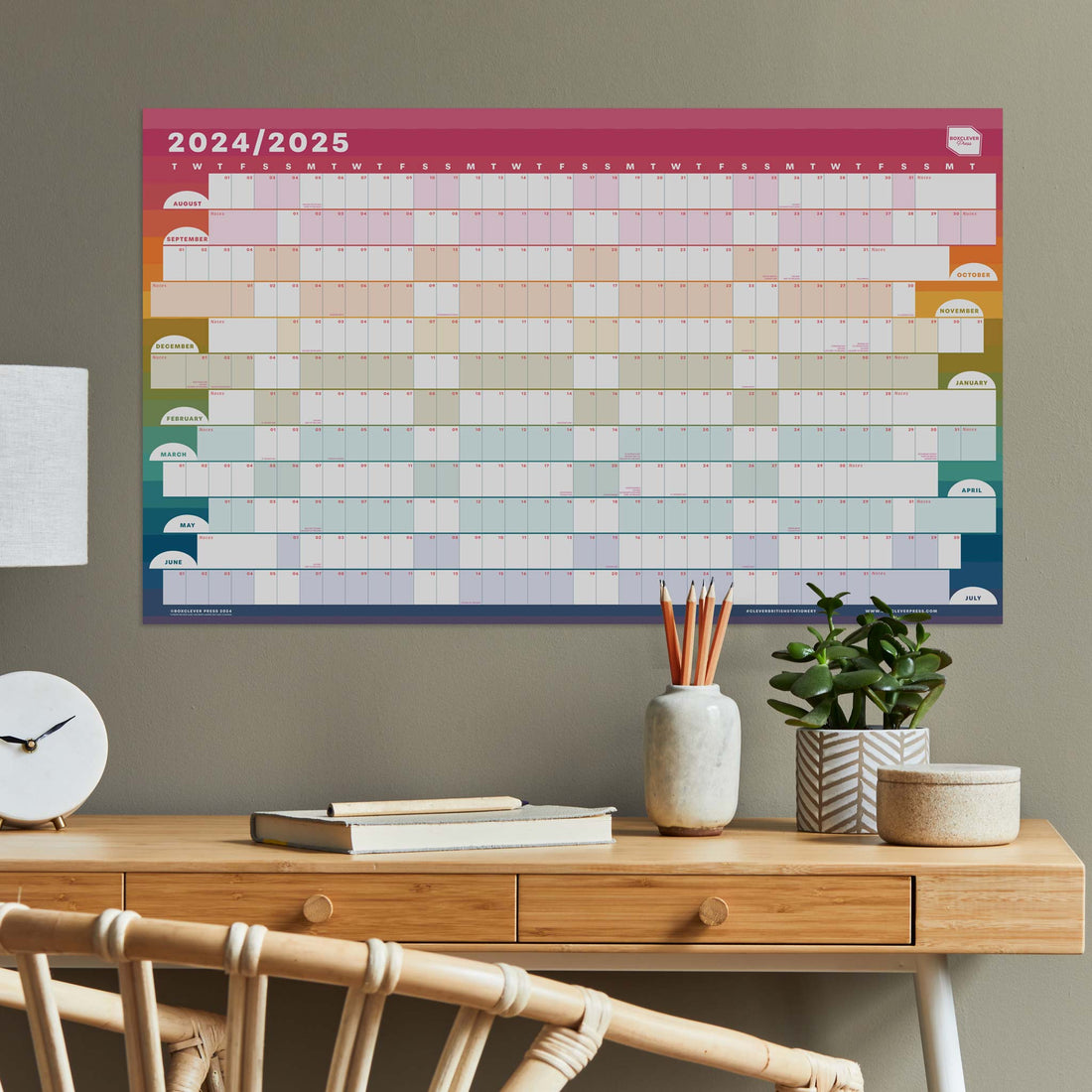 Academic wall planner with rainbow design hung above a wooden table